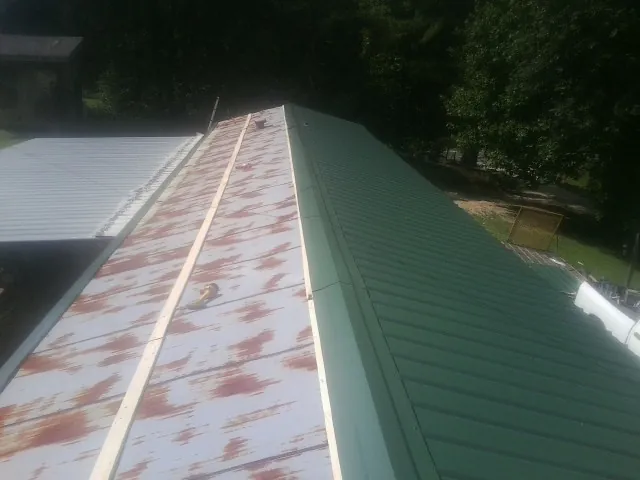 Old rusted panels beside newly installed green metal roofing — Wind Damage Roof Repair by Roofing Brothers in Brandon